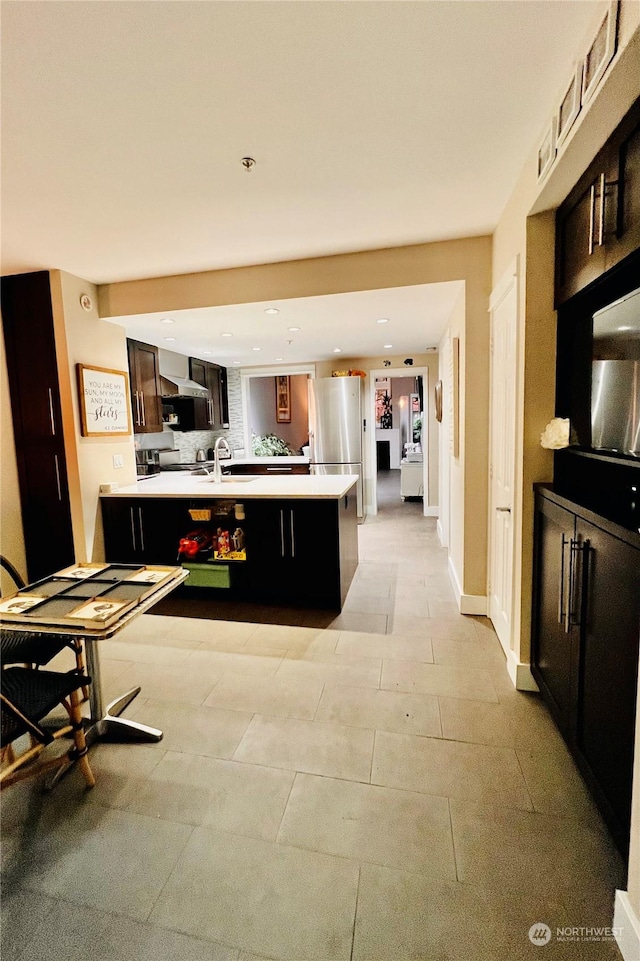 kitchen featuring sink, a kitchen island with sink, decorative backsplash, and stainless steel fridge