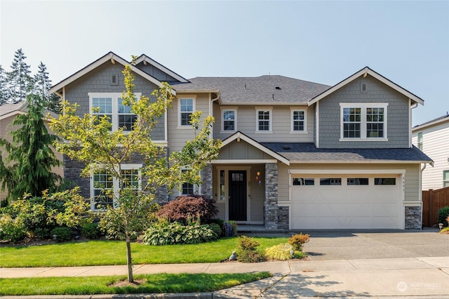 craftsman-style house with driveway, roof with shingles, an attached garage, a front lawn, and stone siding