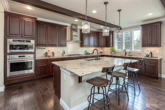 kitchen with tasteful backsplash, wall chimney range hood, an island with sink, stainless steel appliances, and a sink