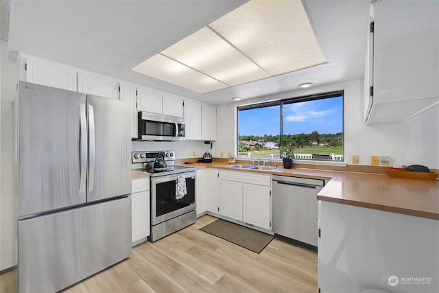 kitchen with sink, light wood-type flooring, white cabinetry, and appliances with stainless steel finishes