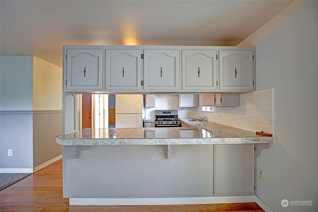 kitchen with sink, white refrigerator, stainless steel range with gas cooktop, kitchen peninsula, and white cabinets