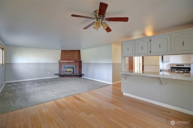 unfurnished living room with ceiling fan, a fireplace, and light wood-type flooring