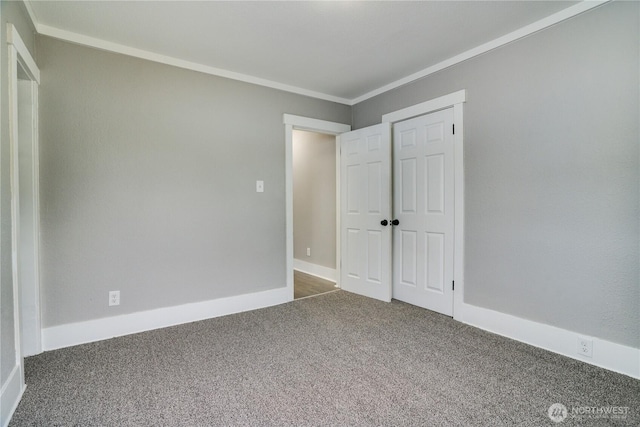 unfurnished bedroom featuring carpet flooring, ornamental molding, baseboards, and a closet