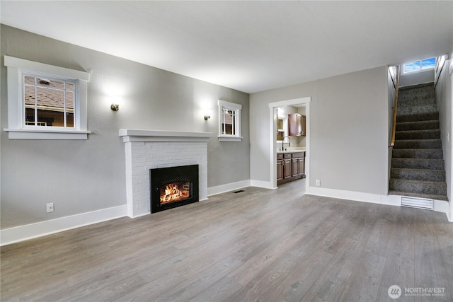 unfurnished living room with wood finished floors, baseboards, a brick fireplace, and stairway