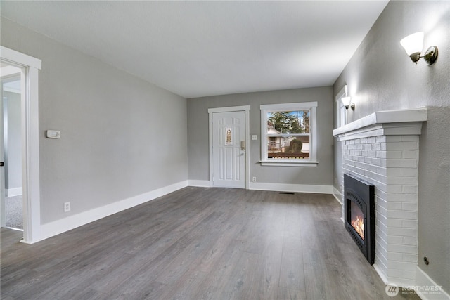 unfurnished living room featuring a brick fireplace, dark wood-style floors, and baseboards