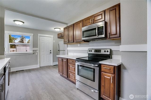kitchen featuring stainless steel appliances, light wood-type flooring, light countertops, and brown cabinets