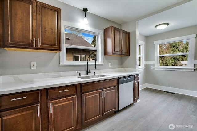 kitchen featuring stainless steel dishwasher, a sink, light wood finished floors, baseboards, and light stone counters