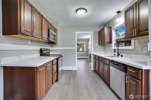 kitchen with appliances with stainless steel finishes, a sink, light wood finished floors, light countertops, and baseboards