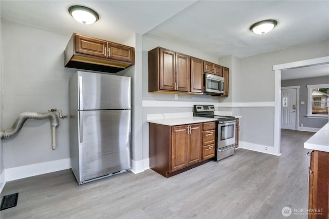 kitchen with appliances with stainless steel finishes, light wood-type flooring, baseboards, light countertops, and brown cabinets