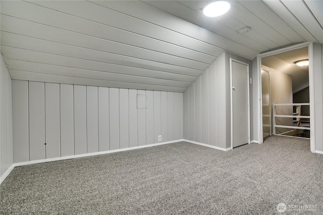 additional living space featuring carpet, lofted ceiling, and wood walls