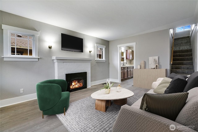 living room with baseboards, stairway, light wood-style floors, and a brick fireplace