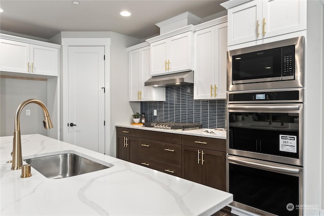 kitchen featuring backsplash, sink, white cabinetry, stainless steel appliances, and light stone counters