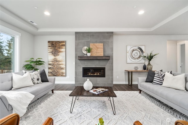 living room featuring hardwood / wood-style floors, a raised ceiling, and a tiled fireplace