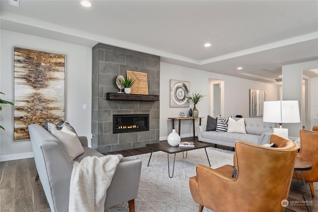 living room with a raised ceiling, a tiled fireplace, and hardwood / wood-style flooring