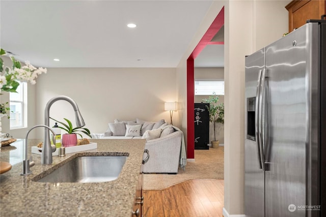 kitchen featuring stainless steel refrigerator with ice dispenser, wood-type flooring, sink, and light stone counters