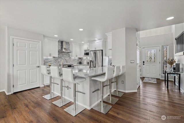 kitchen featuring wall chimney exhaust hood, a breakfast bar, high end refrigerator, kitchen peninsula, and white cabinets