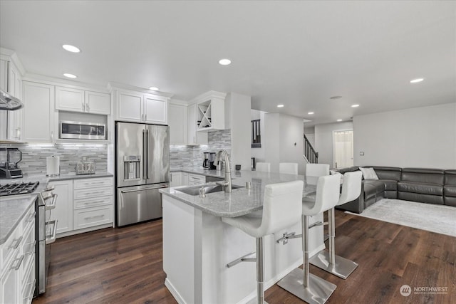 kitchen featuring sink, appliances with stainless steel finishes, light stone countertops, white cabinets, and a kitchen bar