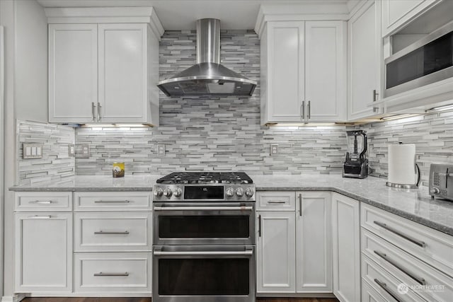 kitchen featuring tasteful backsplash, white cabinets, appliances with stainless steel finishes, and wall chimney range hood