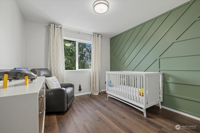 bedroom featuring a nursery area, wooden walls, and dark wood-type flooring