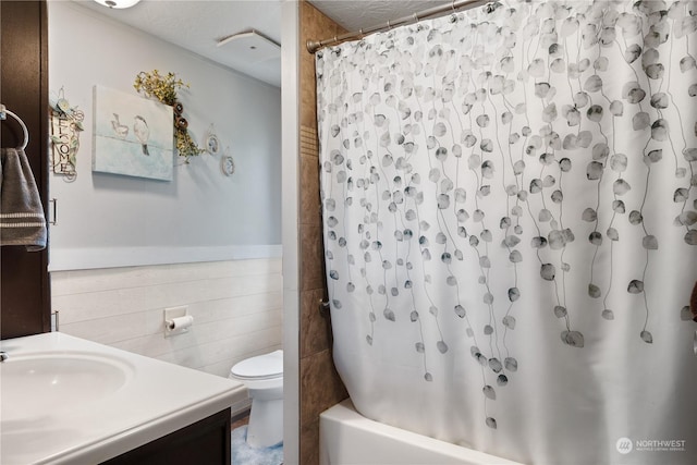 full bathroom featuring a textured ceiling, vanity, shower / bath combination with curtain, tile walls, and toilet