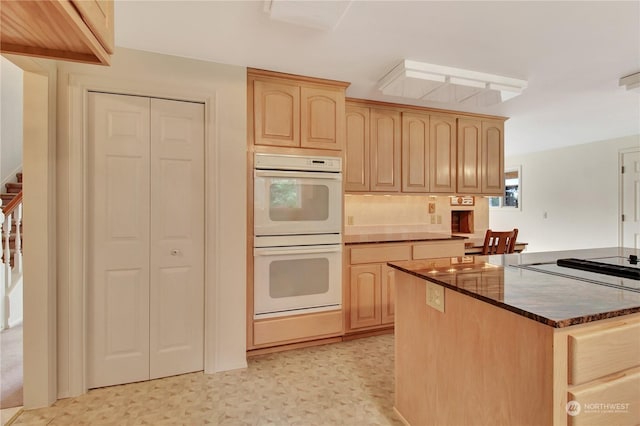 kitchen with white double oven, light brown cabinets, and dark stone counters