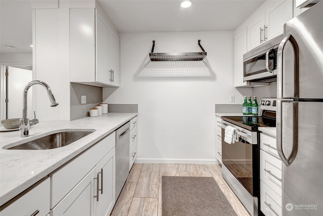 kitchen with white cabinetry, appliances with stainless steel finishes, light stone countertops, and sink