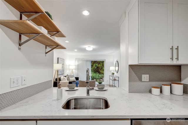 kitchen with light stone counters, sink, tasteful backsplash, and white cabinets