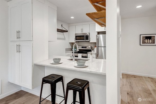 kitchen featuring a kitchen bar, sink, light stone counters, appliances with stainless steel finishes, and white cabinets