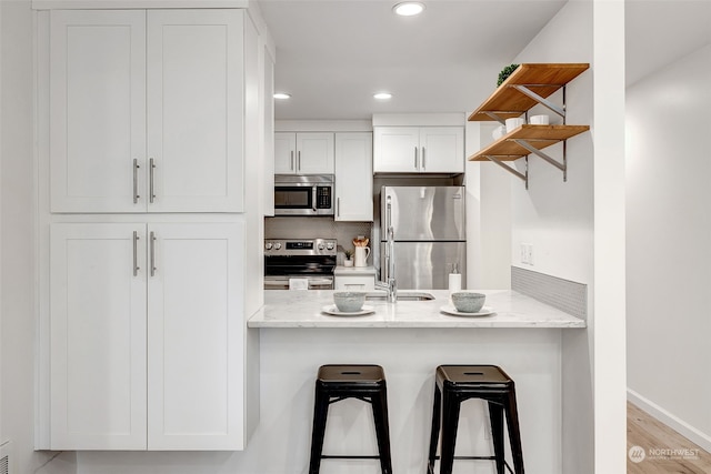 kitchen with a breakfast bar area, white cabinetry, light hardwood / wood-style flooring, appliances with stainless steel finishes, and light stone countertops