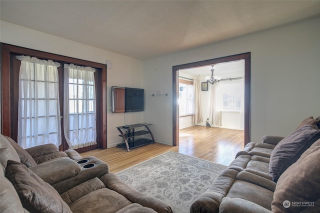 living room featuring an inviting chandelier, light wood-style flooring, baseboards, and a wealth of natural light