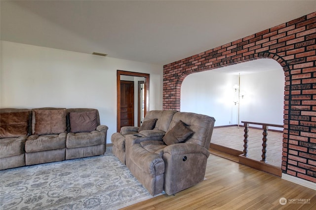 living area with arched walkways, visible vents, light wood-style flooring, and brick wall