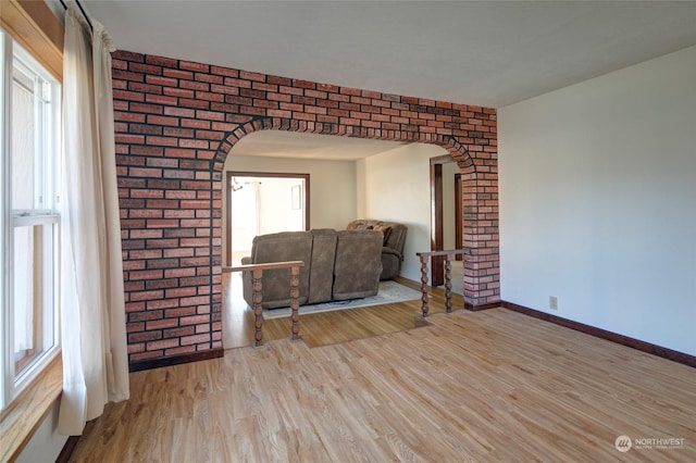 unfurnished living room featuring brick wall and light wood-type flooring