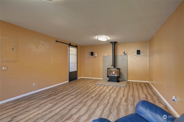 unfurnished living room with a wood stove, electric panel, a barn door, and wood-type flooring