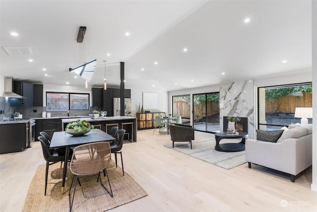 dining area with a premium fireplace, light hardwood / wood-style flooring, and lofted ceiling