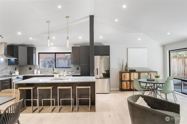 kitchen featuring a center island, vaulted ceiling, decorative light fixtures, stainless steel appliances, and wall chimney exhaust hood