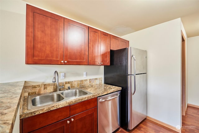 kitchen with stainless steel appliances, light hardwood / wood-style floors, light stone counters, and sink