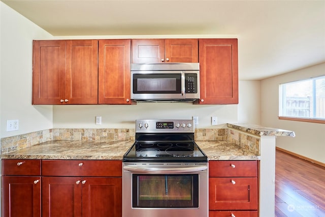 kitchen with appliances with stainless steel finishes, hardwood / wood-style floors, and light stone countertops