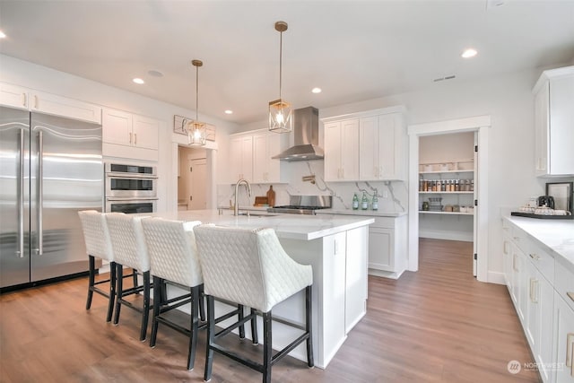 kitchen with wall chimney range hood, stainless steel appliances, and white cabinets