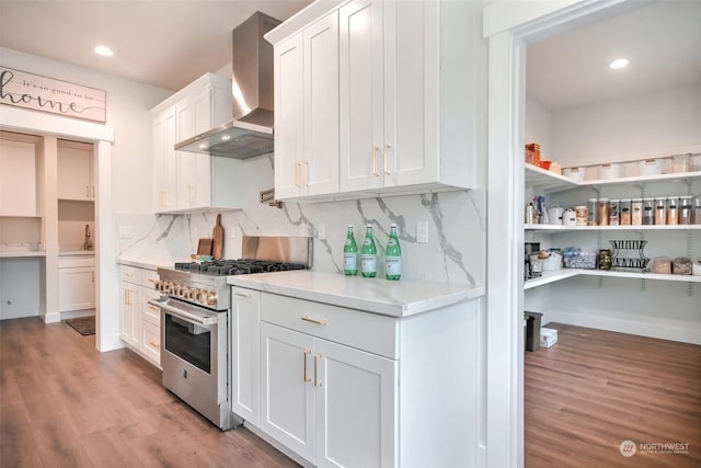 kitchen featuring wall chimney exhaust hood, high end stainless steel range, light wood-type flooring, decorative backsplash, and white cabinets