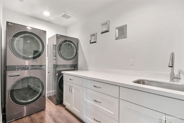 clothes washing area with stacked washer / drying machine, hardwood / wood-style flooring, cabinets, and sink