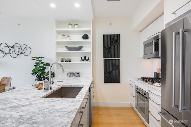 kitchen with sink, white cabinets, stainless steel appliances, light stone countertops, and light wood-type flooring