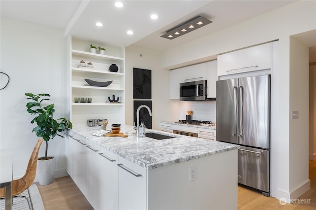 kitchen featuring appliances with stainless steel finishes, sink, white cabinets, light stone counters, and kitchen peninsula