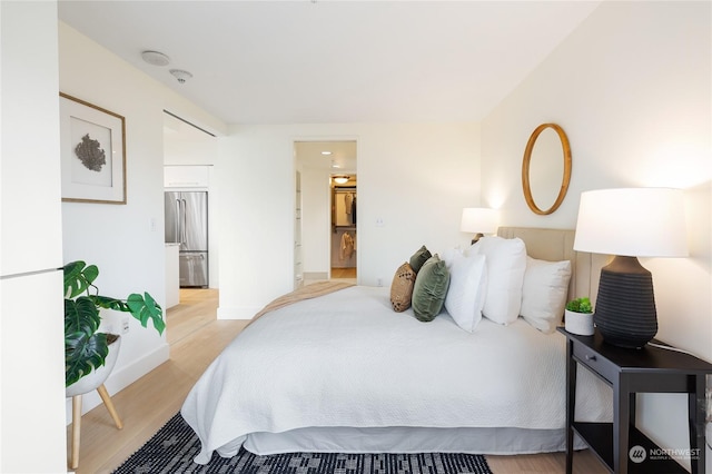 bedroom with stainless steel refrigerator, ensuite bath, and light hardwood / wood-style floors