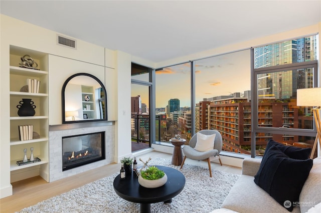 living room featuring plenty of natural light, built in features, a high end fireplace, and light hardwood / wood-style floors