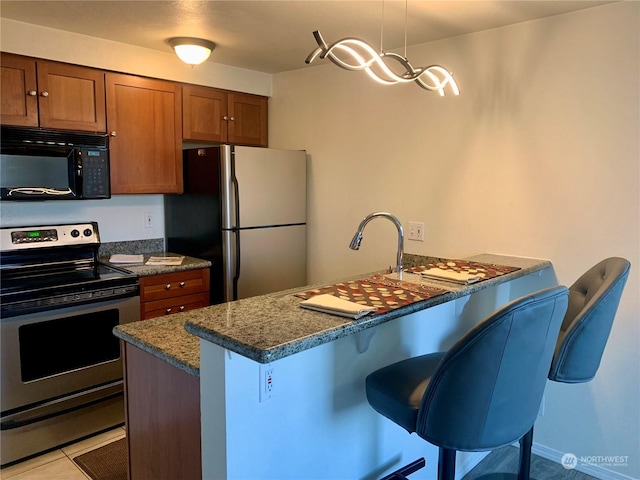 kitchen featuring a kitchen breakfast bar, appliances with stainless steel finishes, decorative light fixtures, dark stone counters, and light tile patterned flooring