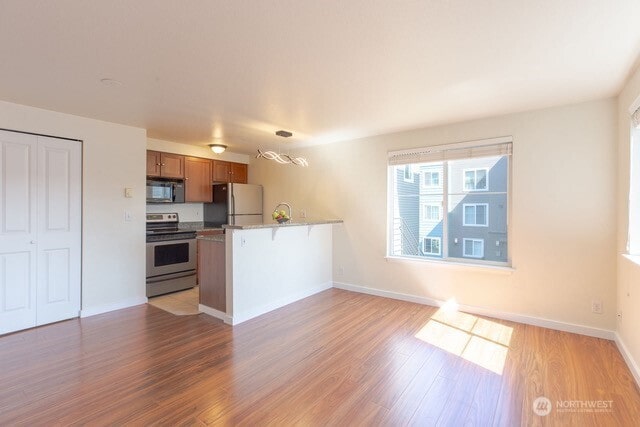 300 10th Ave Unit A203, Seattle, WA 98122 - kitchen with stainless steel appliances, brown cabinets, a peninsula, light wood-type flooring, and a kitchen bar