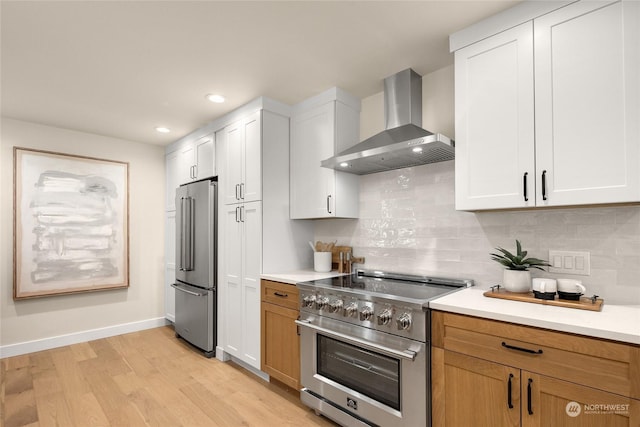 kitchen featuring white cabinetry, light hardwood / wood-style flooring, premium appliances, wall chimney range hood, and backsplash