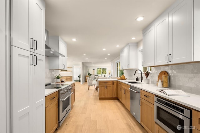 kitchen featuring appliances with stainless steel finishes, sink, white cabinets, kitchen peninsula, and wall chimney exhaust hood