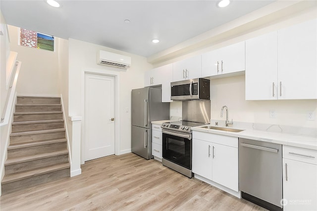 kitchen featuring sink, a wall mounted AC, light hardwood / wood-style flooring, appliances with stainless steel finishes, and white cabinets