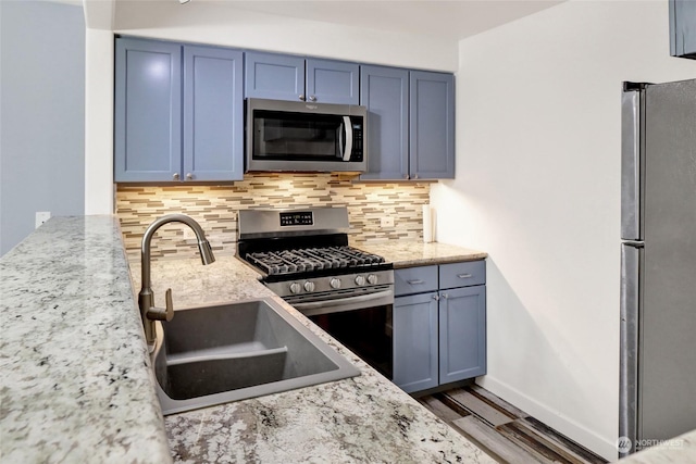 kitchen with decorative backsplash, sink, light stone countertops, appliances with stainless steel finishes, and blue cabinets